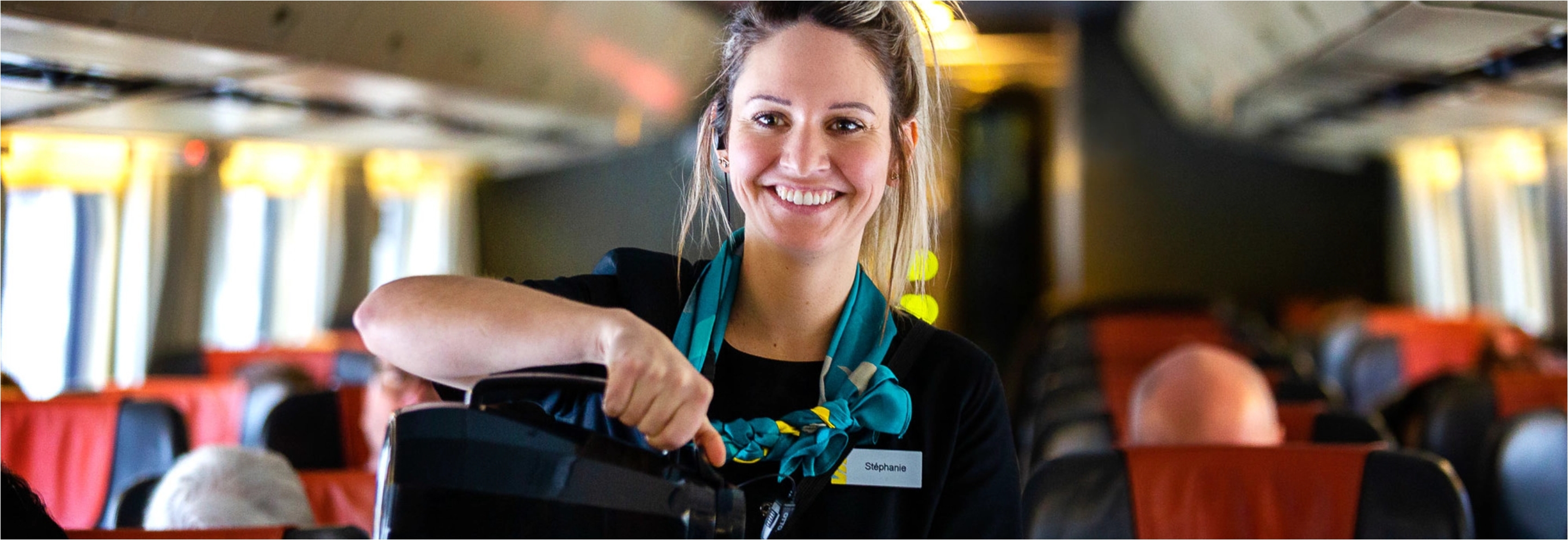 Employée VIA Rail souriant et versant du café dans une tasse à bord d’un train