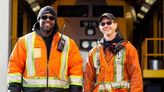 Deux employés de VIA Rail en tenue de sécurité devant un train